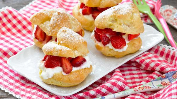 windbeutel aus brandteig mit erdbeeren und sahne auf einem tablett mit rot-weißer tischdecke