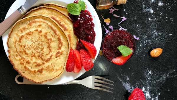 pancakes auf einem teller mit beeren auf einer schwarzen tischplatte von oben