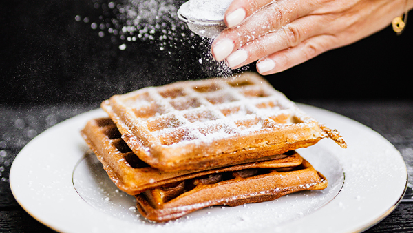 hier werden waffeln mit puderzucker bestreut auf einem weißen teller